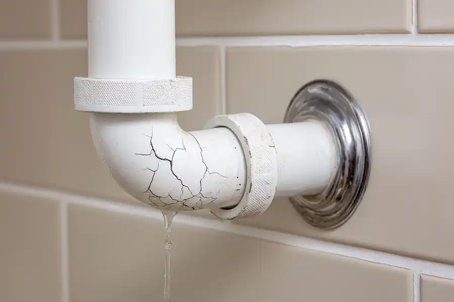 F.J. Murphy & Son, Inc. — A cracked white pipe leaking water against a tiled wall in a bathroom in a residential Springfield, IL home.