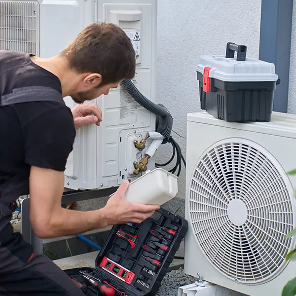 Technician servicing outdoor heat pump unit with tools beside residential house Athens IL